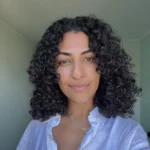 Bild von Nieki Hashemi, Teammitglied von TeleClinic. Junge Frau mit dunklen, lockigen Haaren und braunen Augen lächelt in die Kamera.