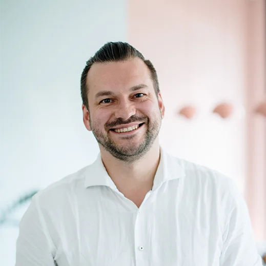 Bild von Adrian Schneider. Teammitglied von TeleClinic. Freundlich blickender Mann mit dunklen Haaren und Bart innerhalb eines TeleClinic Bürogebäudes.