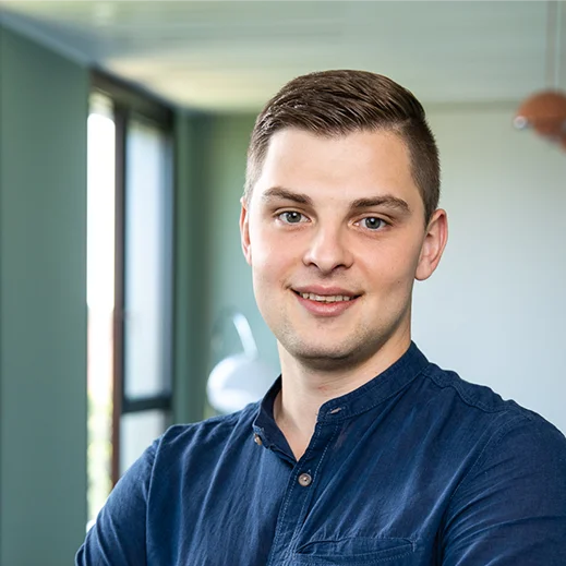 Bild von Julian Dittel. Teammitglied von TeleClinic. Freundlich blickender junger Mann mit braunen Haaren innerhalb eines TeleClinic Bürogebäudes.