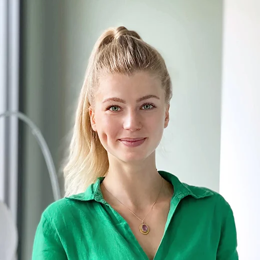 Bild von Johanna Stockdreher. Teammitglied von TeleClinic. Freundlich blickende junge Frau mit blonden Haaren und Zopf innerhalb eines TeleClinic Bürogebäudes.