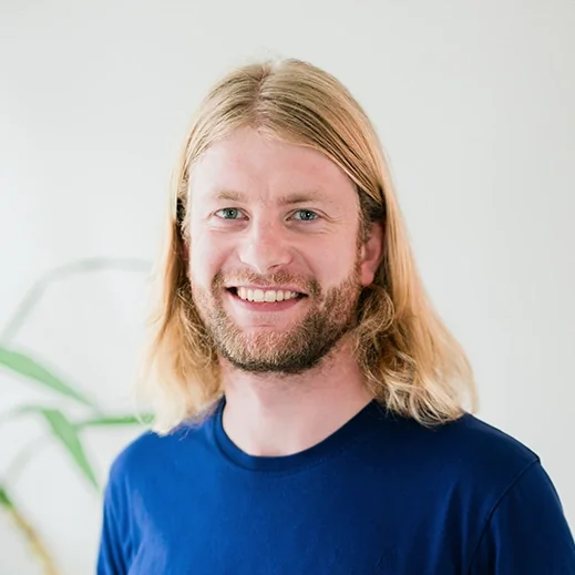 Bild von Jakob Dettmar, TeleClinic Teammitglied. Junger Mann mit längeren hellen Haaren und Bart lächelt in die Kamera.