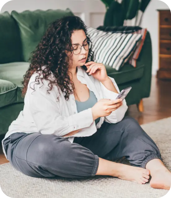Junge Frau die auf dem Boden sitzt und ein Smartphone in der Hand hält.