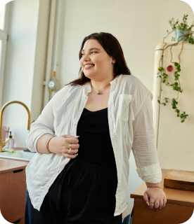 Selbstbewusste Frau, die sich lächelnd mit einem Glas an eine Küchentheke lehnt.