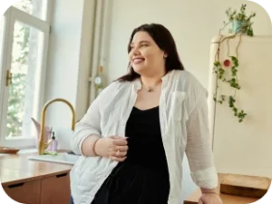 Selbstbewusste Frau, die sich lächelnd mit einem Glas an eine Küchentheke lehnt.