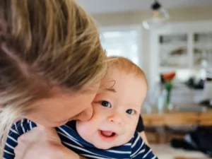 Frau hält lächelndes Baby im Arm, symbolisiert Fürsorge und Familie.