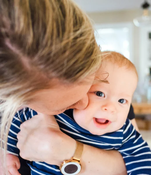 Frau hält lächelndes Baby im Arm, symbolisiert Fürsorge und Familie.