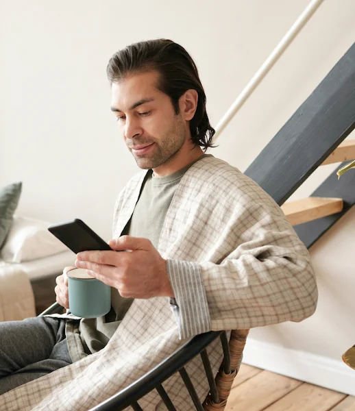 Mann entspannt mit Kaffee und Smartphone, symbolisiert digitale Behandlung von zu Hause.