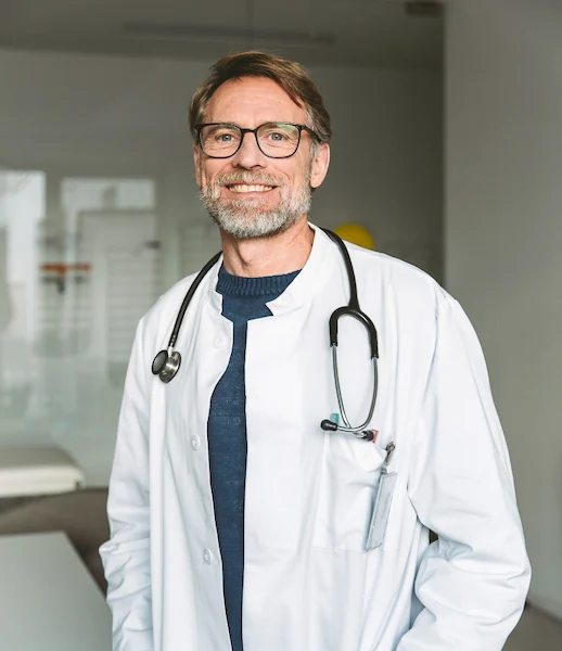 Lächelnder Arzt mit Brille und Stethoskop, symbolisiert Vertrauen und Kompetenz.