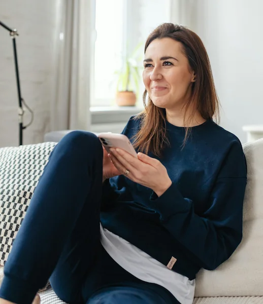 Lächelnde Frau auf Sofa mit Smartphone, symbolisiert Komfort bei digitaler Kommunikation bzw. digitaler Beratung.