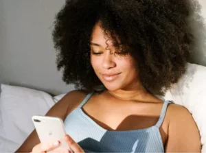 Entspannte Frau im Bett mit Smartphone, symbolisiert bequemen Zugang zu Telemedizin.