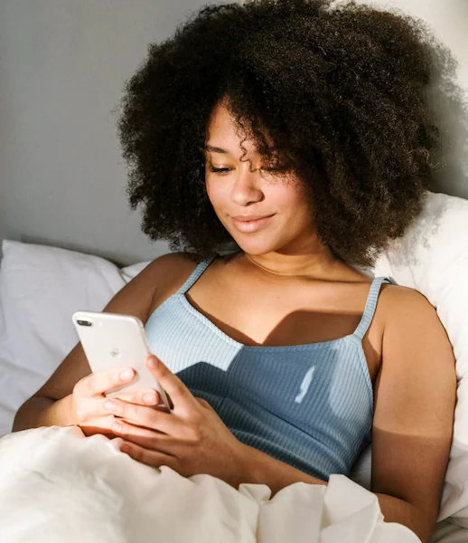 Entspannte Frau im Bett mit Smartphone, symbolisiert bequemen Zugang zu Telemedizin.